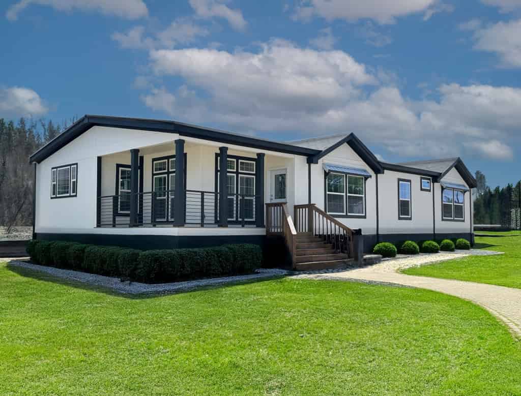 A modern manufactured home with white siding and dark trim on a landscaped lot